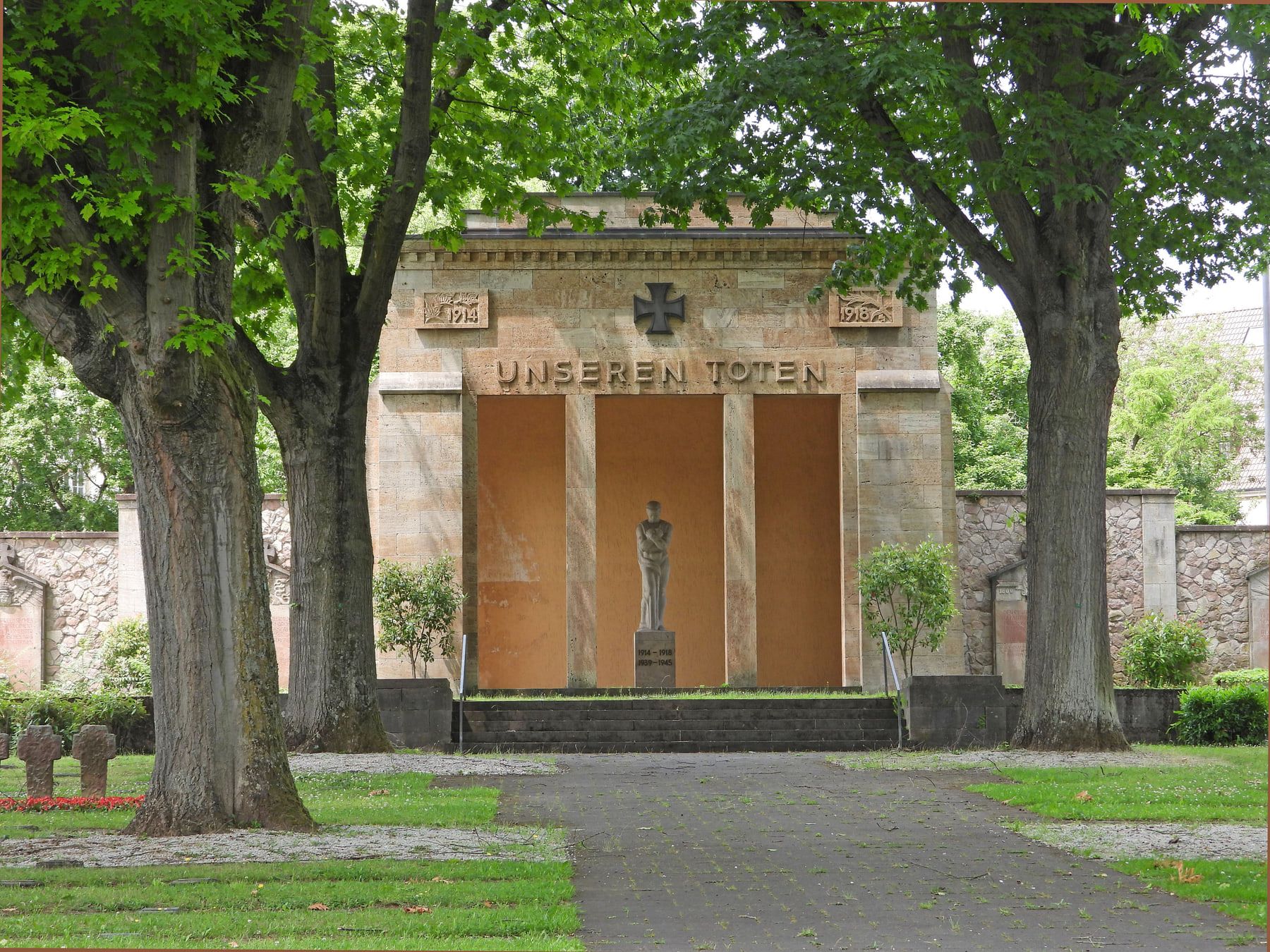 Gedächtnishalle des Deutschen Ehrenhofs zwischen alten Bäumen mit zentraler Figur und der Inschrift „Unseren Toten“ auf Hauptfriedhof Mainz